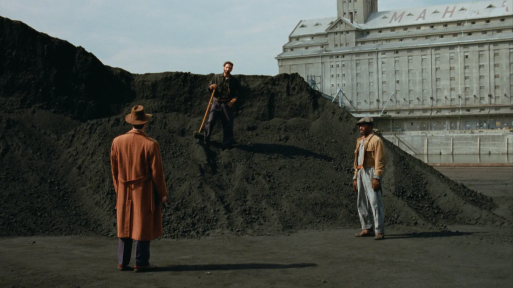 A still from The Brutalist, featuring three figures in wide shot against a Brutalist building