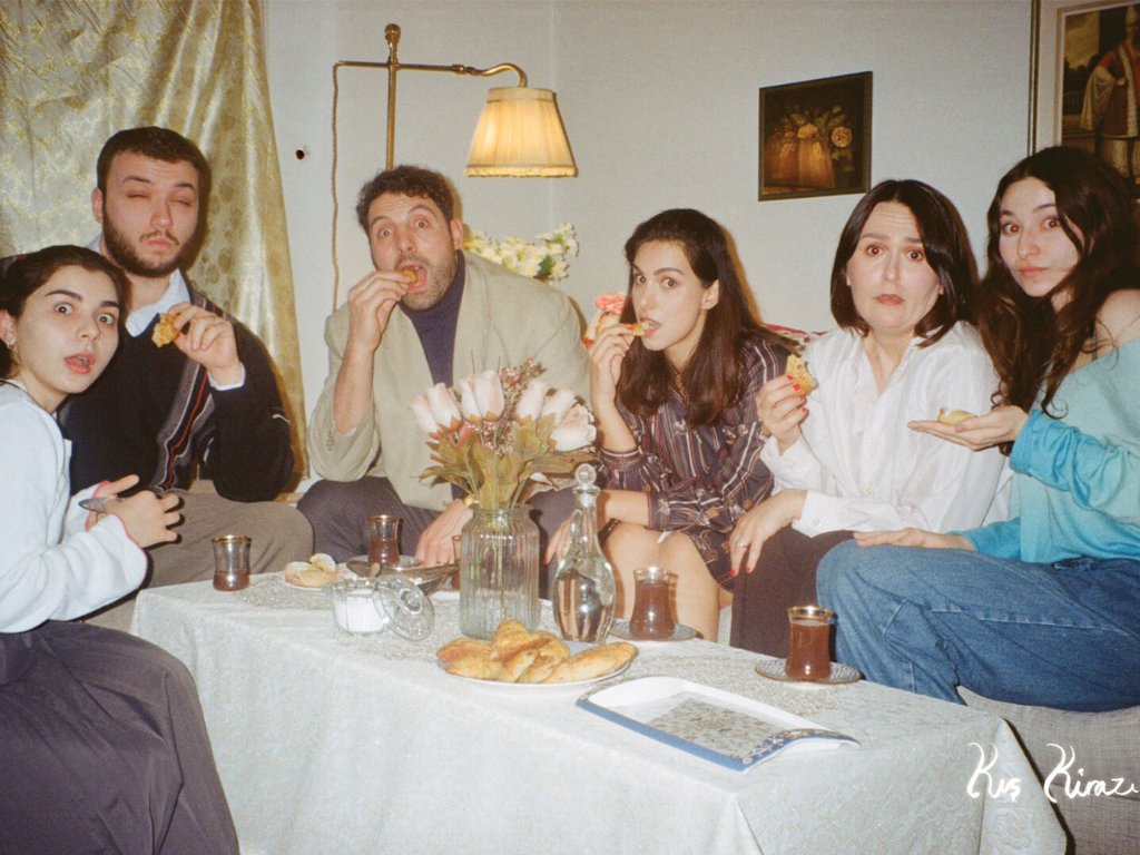 A group of people at a dinner party all look into the camera