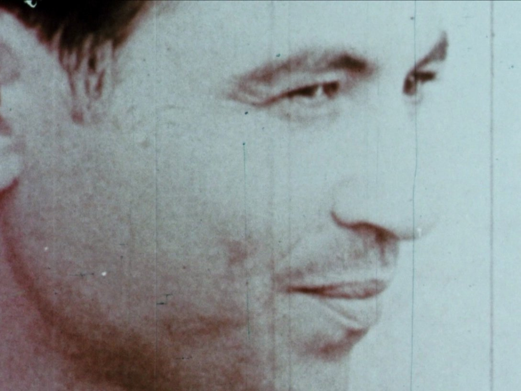 A black and white close-up of a man's side profile. He has dark hair and stands against a light background. 