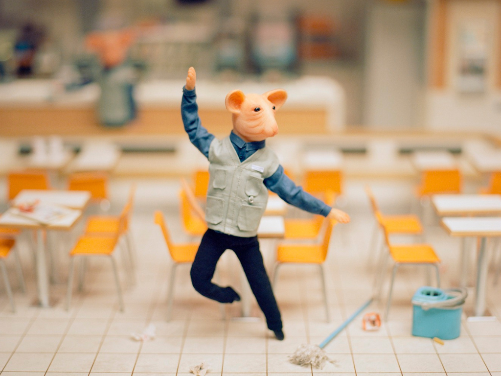 A stop-motion film still of a gerbil wearing a cleaner's uniform and standing on two legs, dancing in a canteen. 