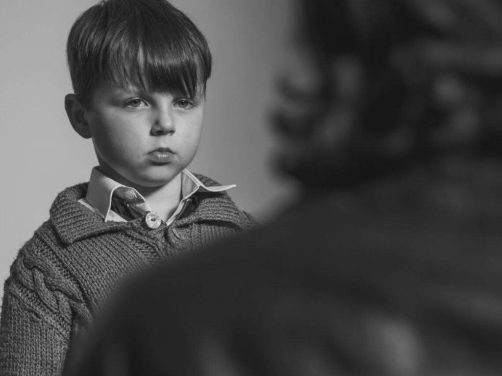 A young boy looks at his father in a black and white still from Lisa Clarkson's Paternal Advice